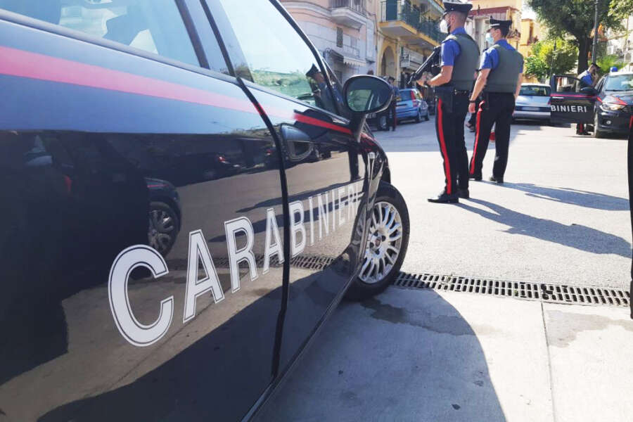 Auto blu con la scritta Carabinieri sul lato destro, due uomini sono in piedi accanto alla portiera