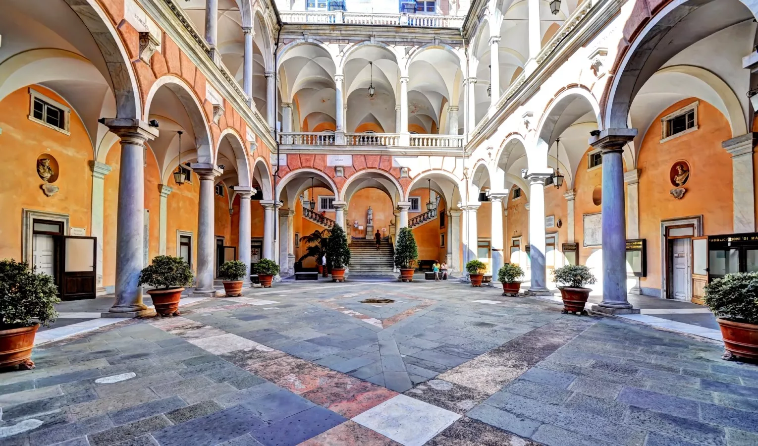 Un piazzale interno di un palazzo con le volte e il sole che illumina