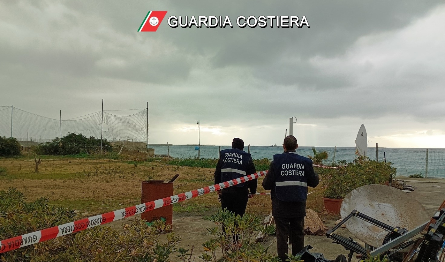 una spiaggia isolata dal nastro bianco e rosso e due uomini di spalle