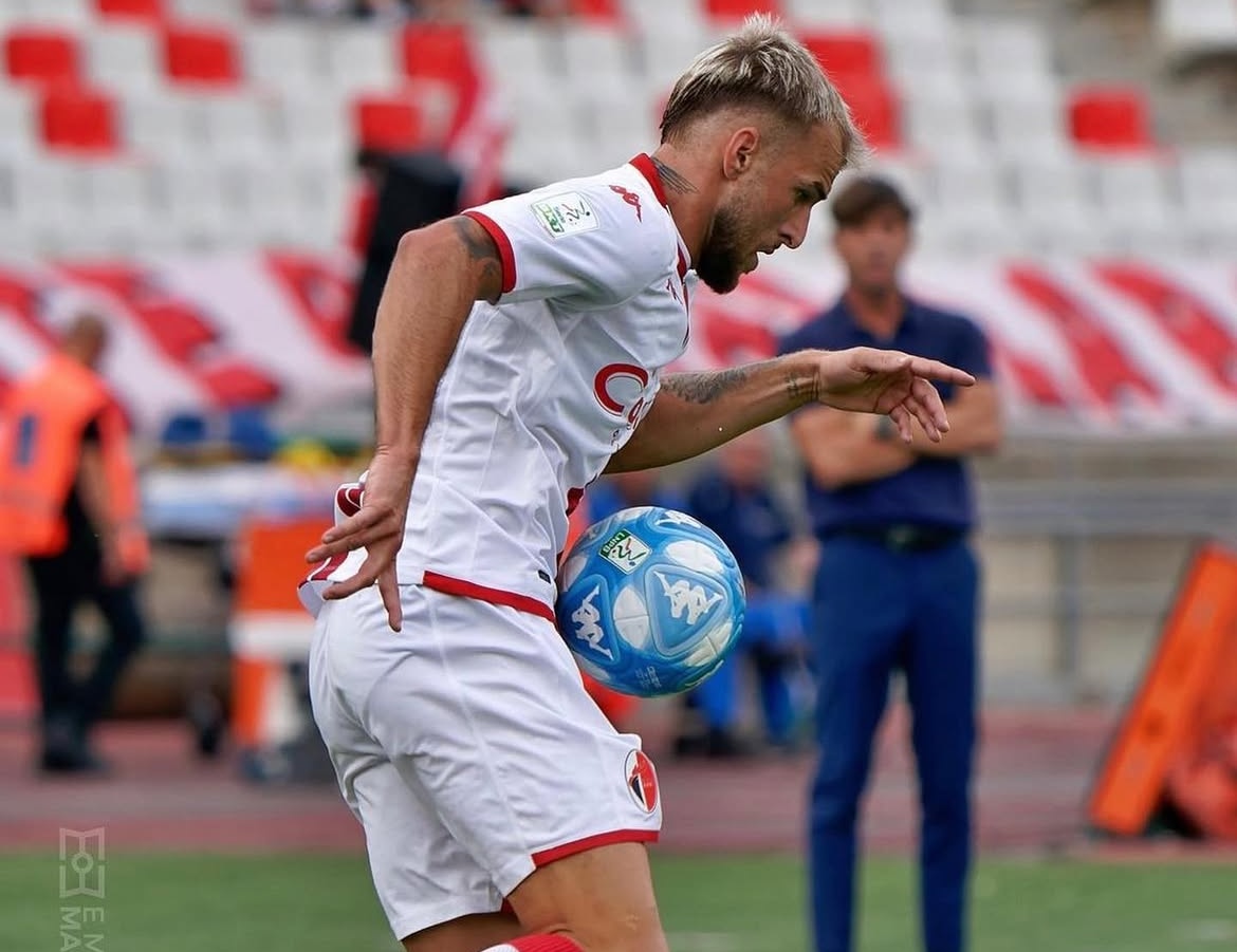 Un calciatore in maglia biancorossa esulta e sorride 