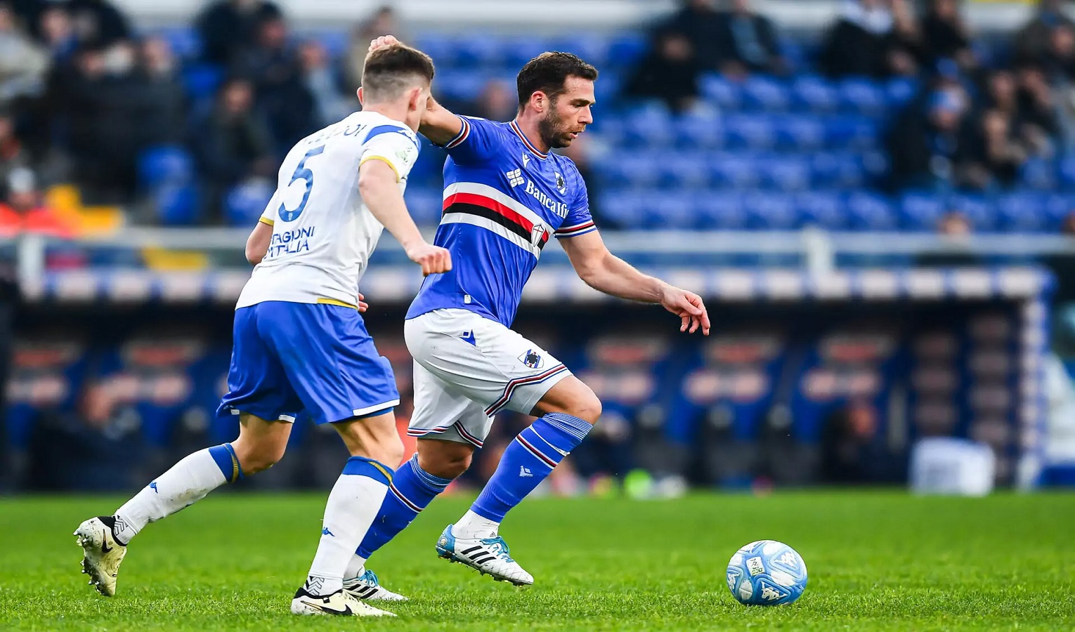 Un calciatore con la maglia della Sampdoria inseguito da un calciatore in maglia bianca