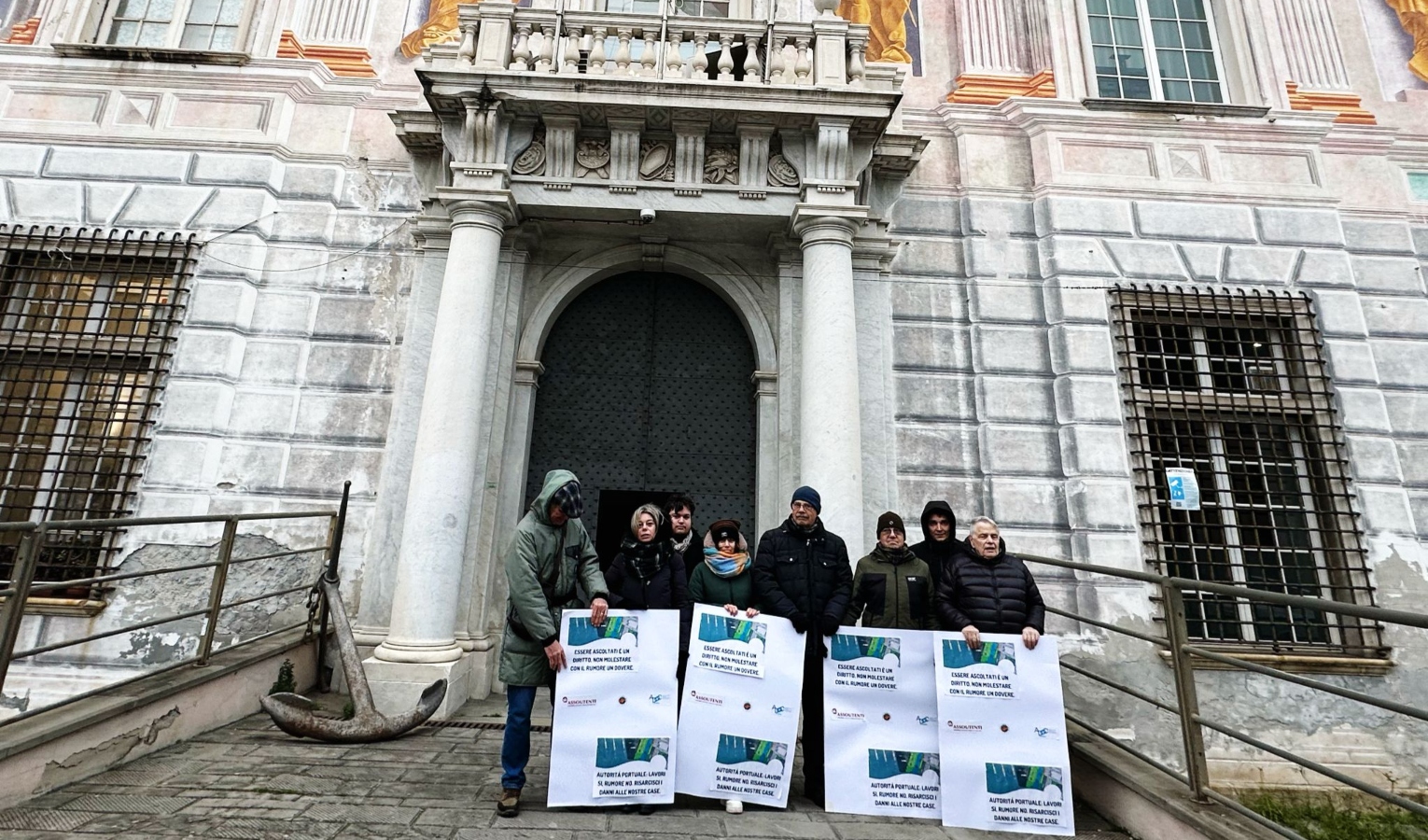 Otto persone con cartelli davanti alla porta di un palazzo storico