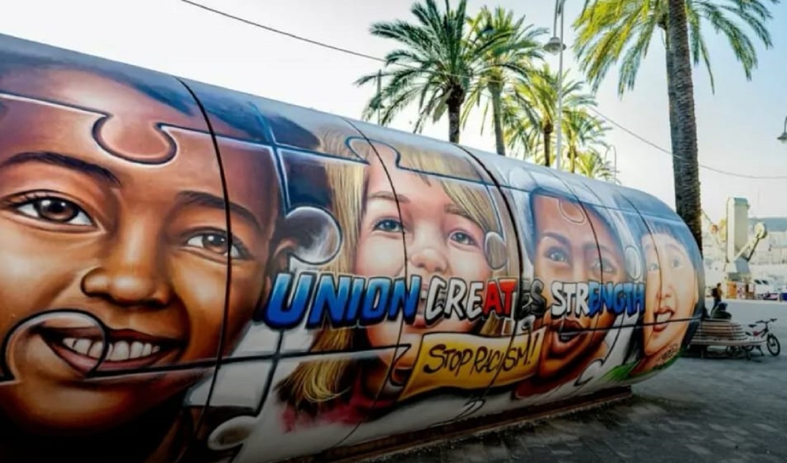 Un murales con facce di bambini di tutto il mondo, un disegno in una piazza con una palma alle spalle