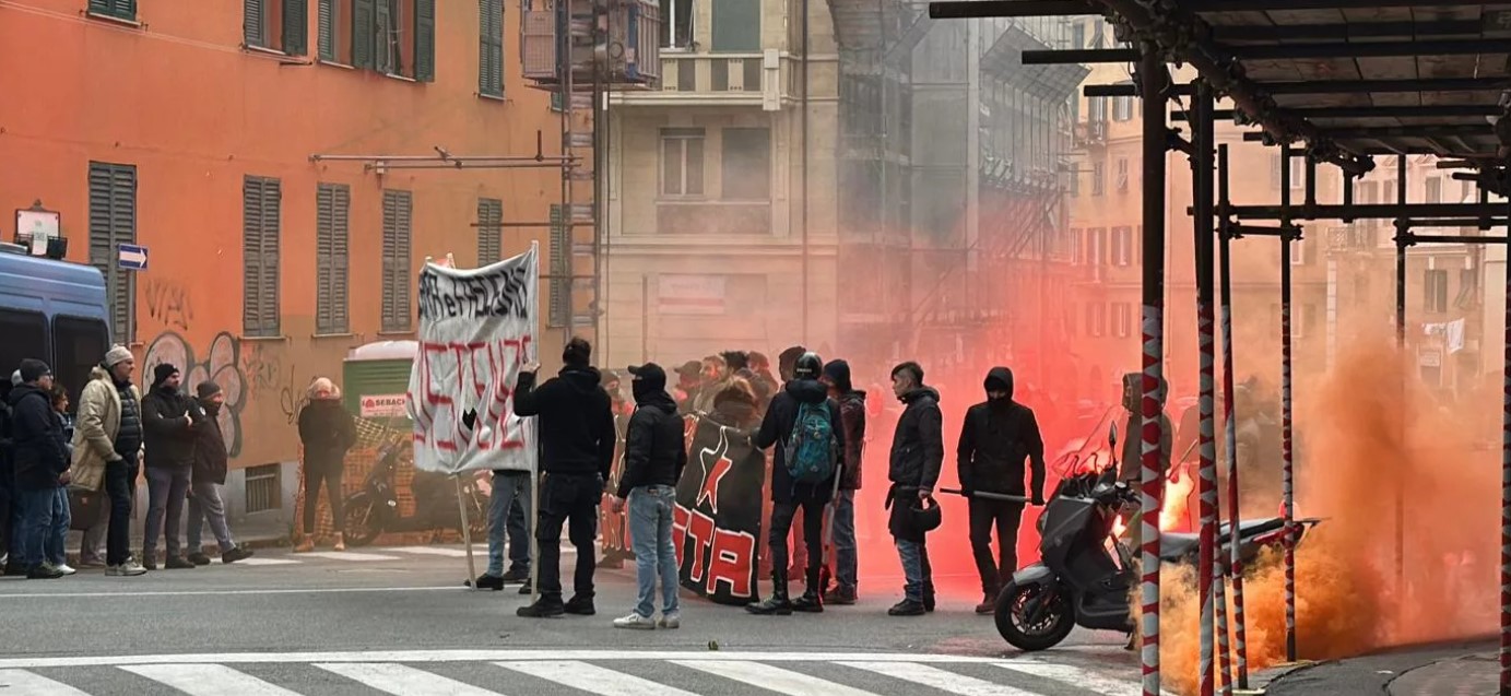 Un gruppetto di persone vestite di scuro con alcune bandiere rosse