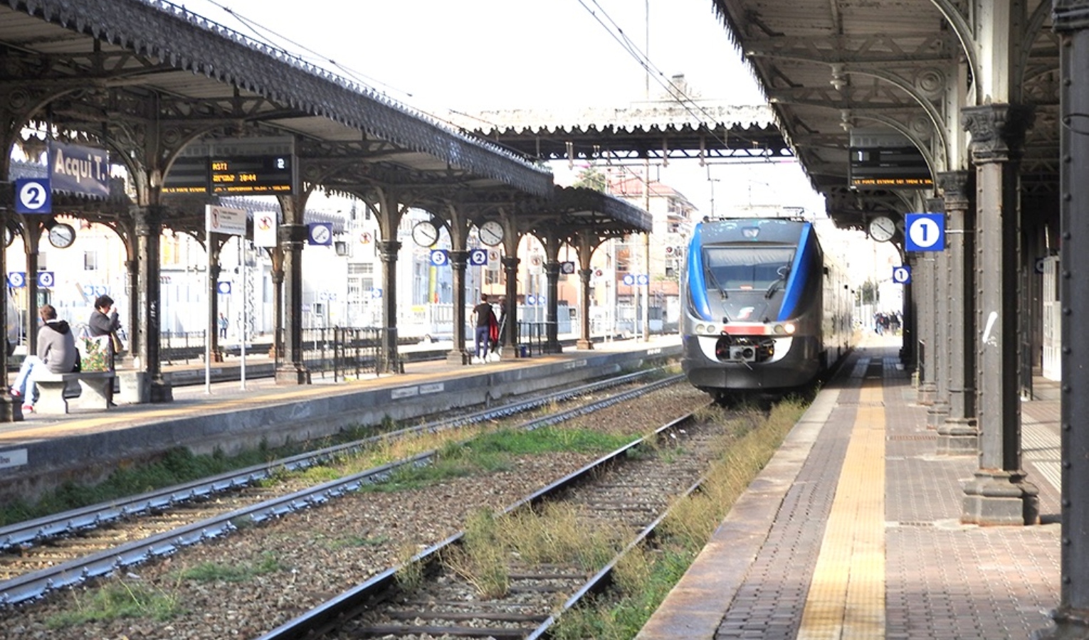 Binari di una stazione e un treno in procinto di avvicinarsi alla fermata