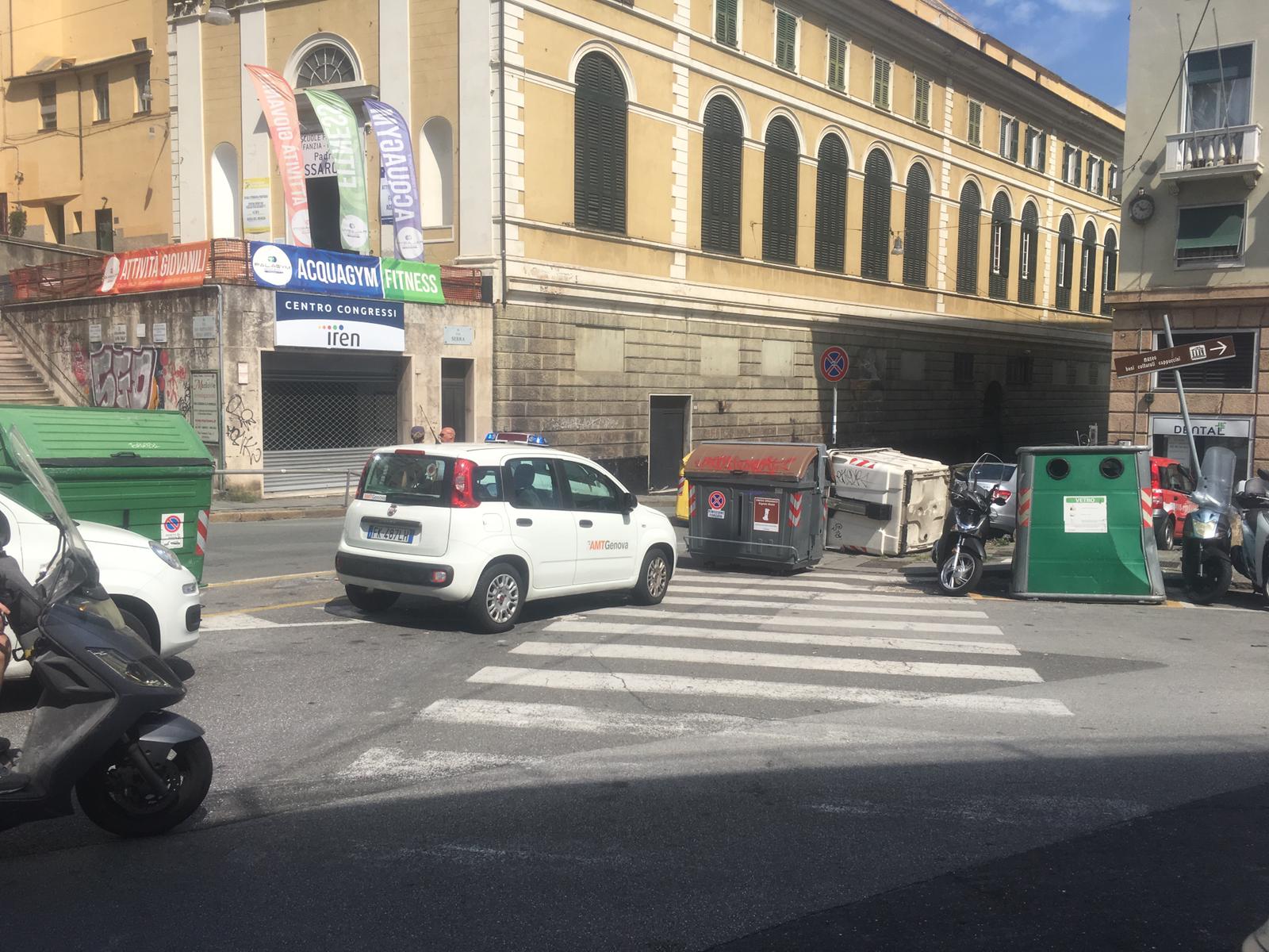 Si stacca il freno a mano, auto travolge i cassonetti e sfiora un bus